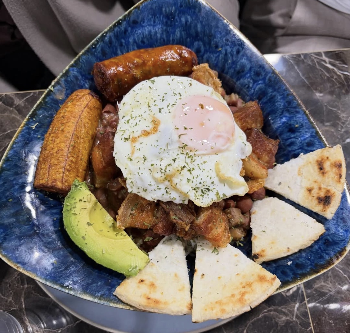 Cazuela de frijoles: red beans and pork belly topped with a fried egg, with chorizo, sweet plantain, avocado and arepa